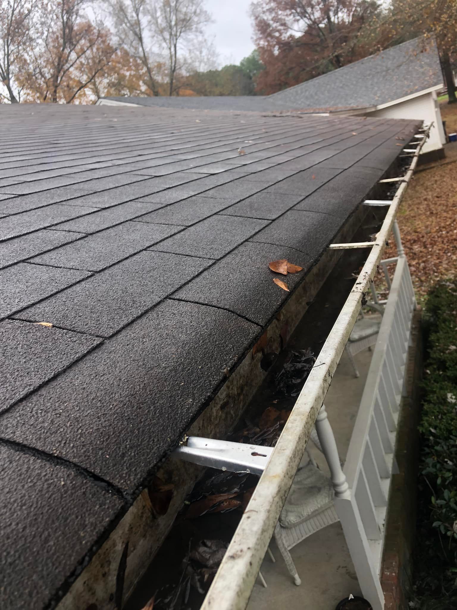 Black shingled roof with a gutter full of debris, viewed from the side. Cloudy day.