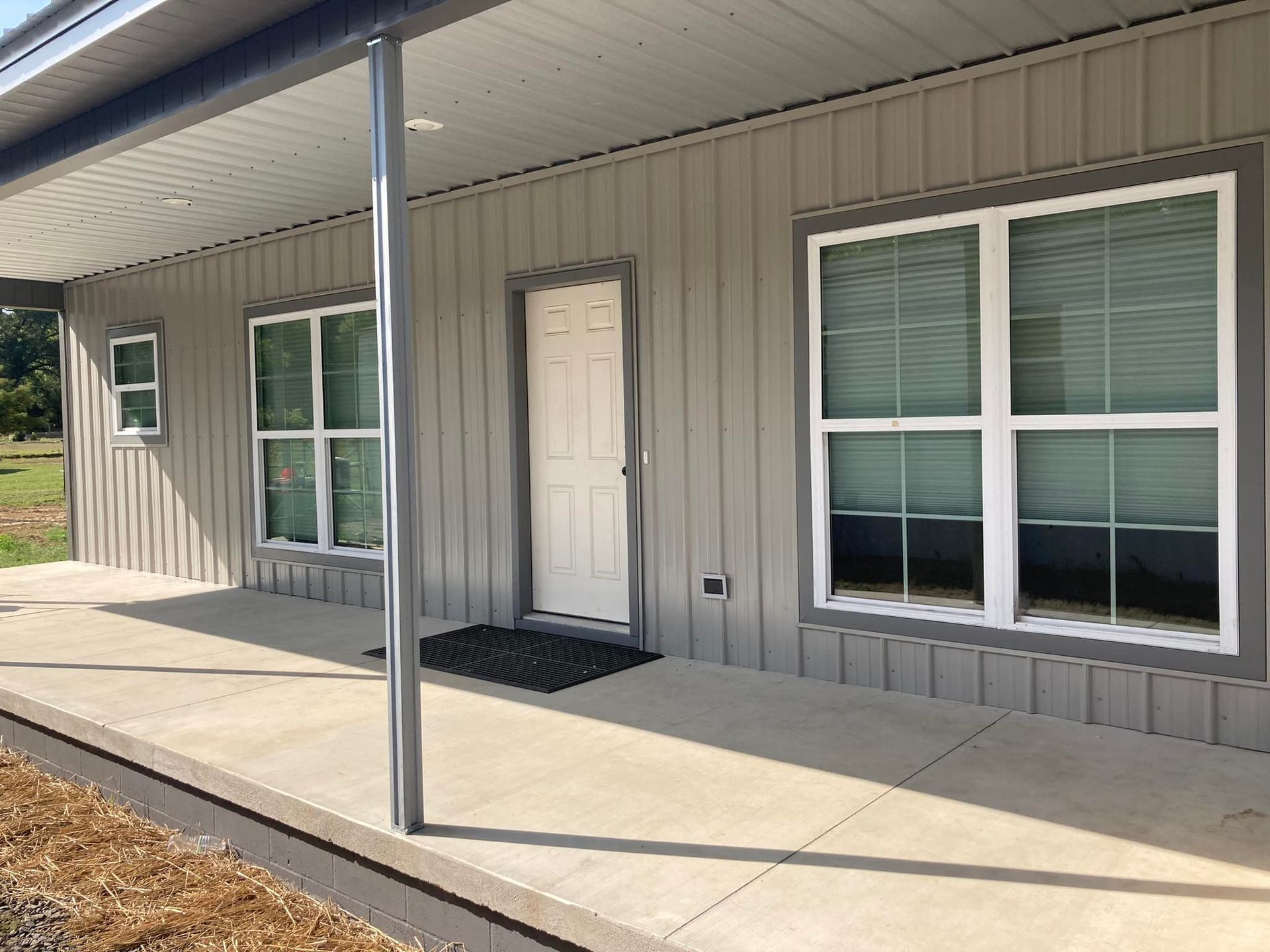 Exterior of a house with gray siding, porch, and windows. White door.