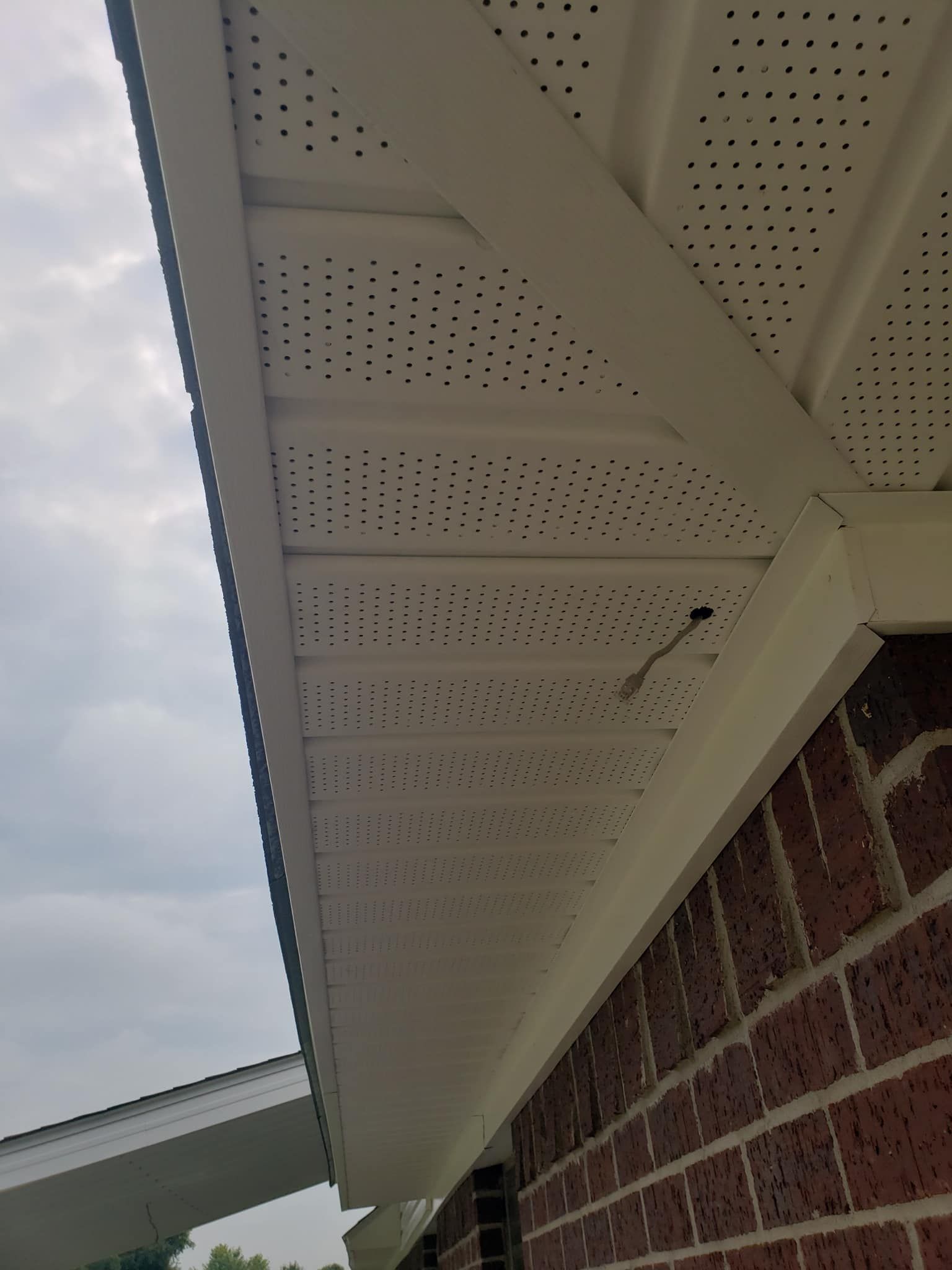 White soffit with ventilation holes on a brick building, viewed from below against a cloudy sky.