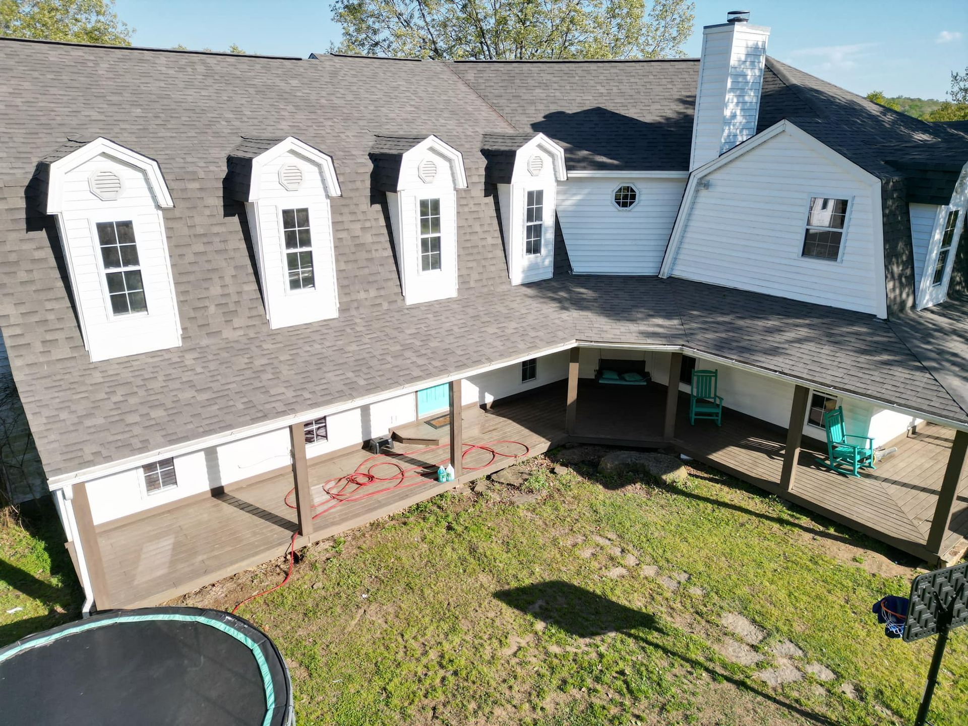 A white house with a gray roof and dormer windows, green lawn, and a trampoline.