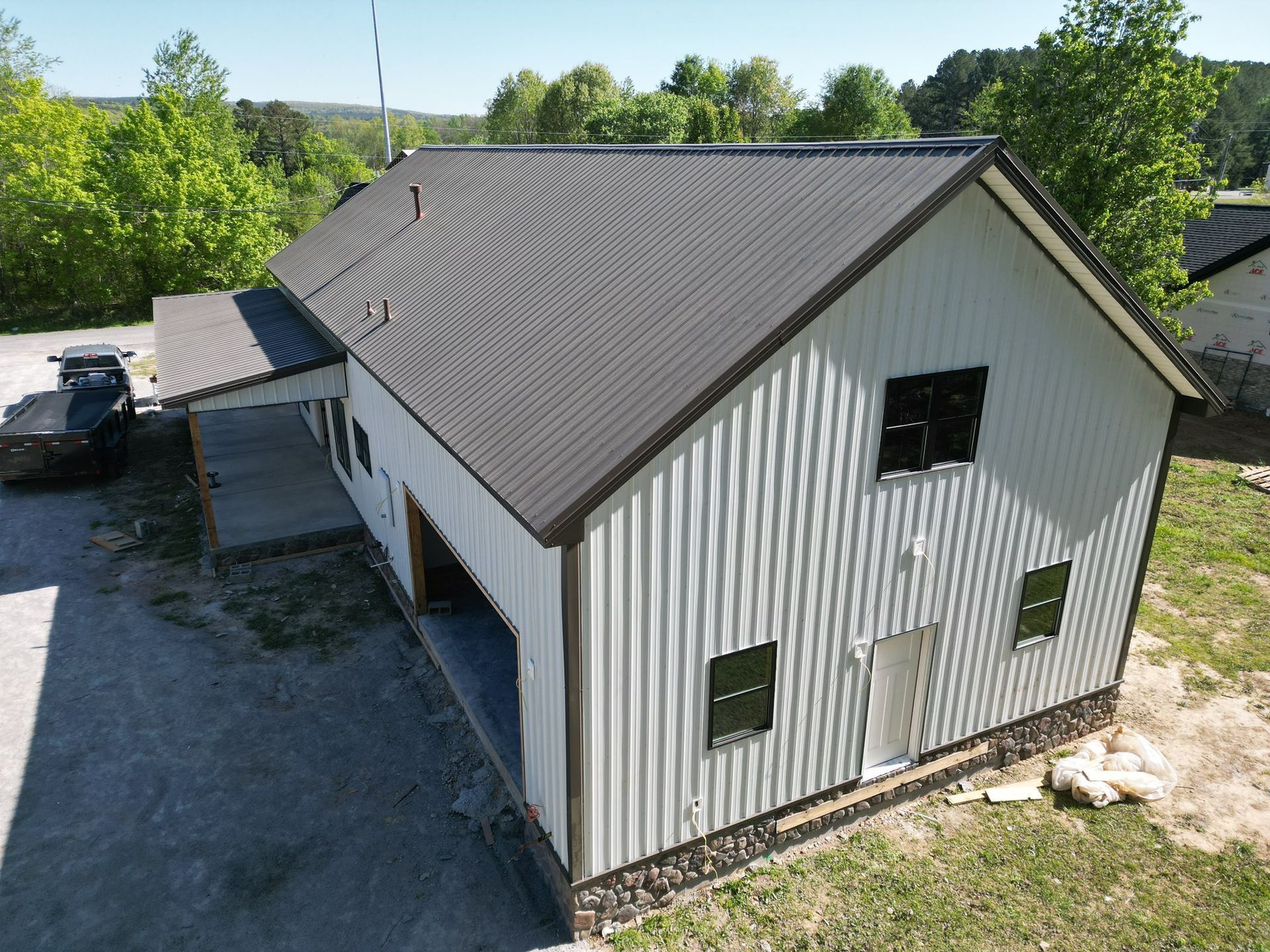 White barn-style building with dark metal roof, open garage doors, and stone base in a sunny outdoor setting.