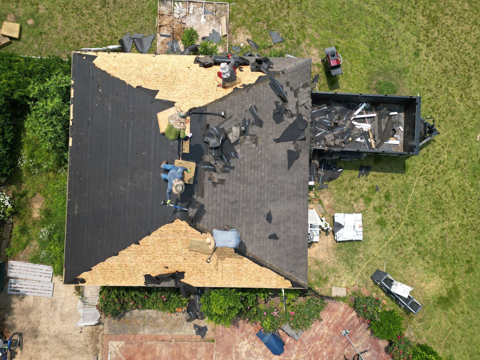 Roofers replacing shingles on a house; part of the roof is uncovered, debris visible, overhead view.