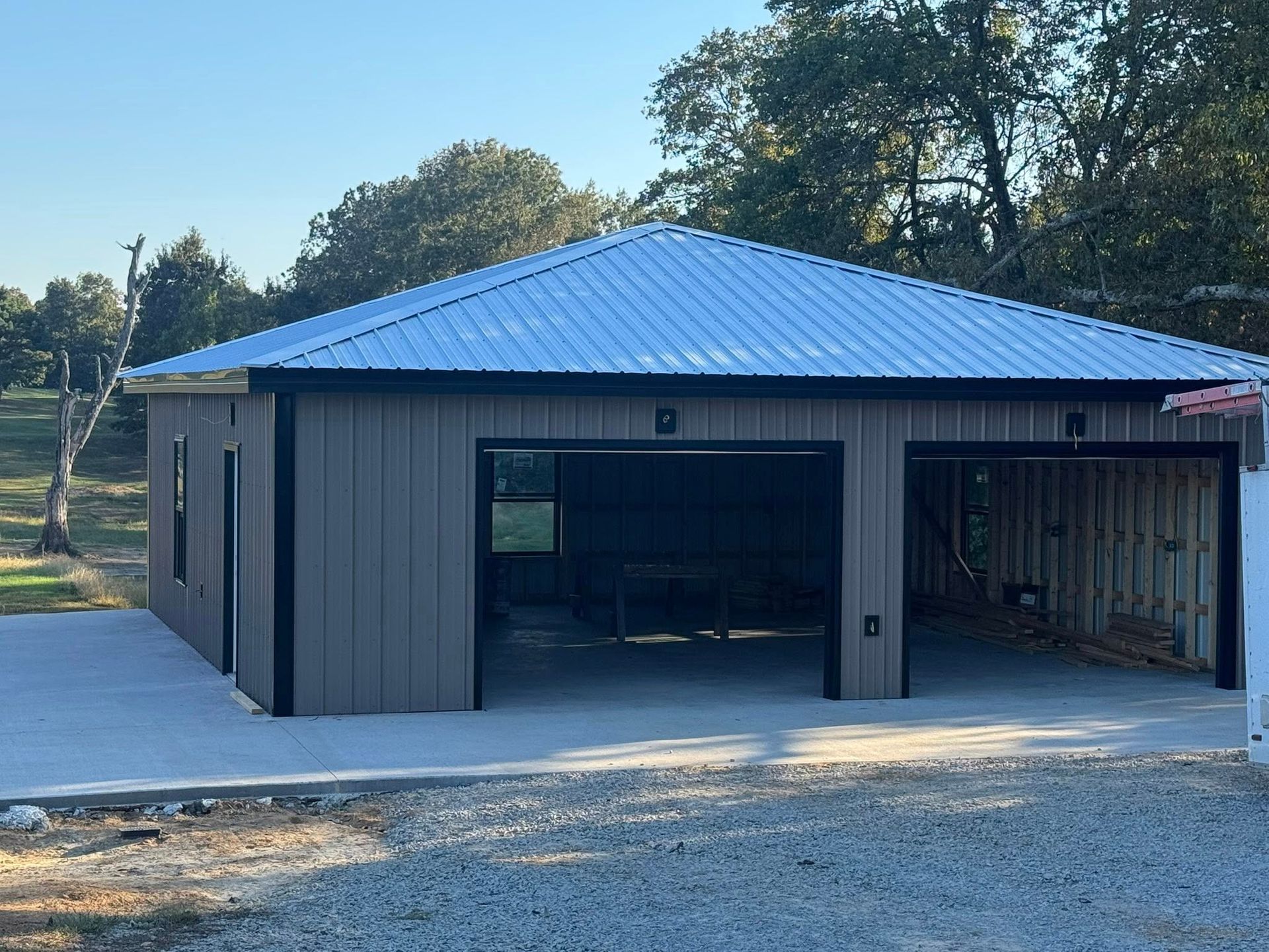 Tan metal garage with a white roof and black trim, two bays open to a concrete pad.