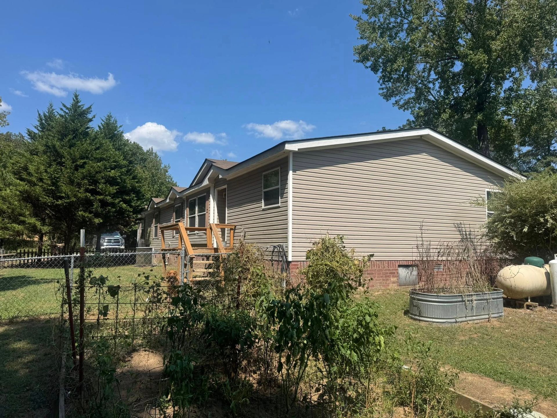 Tan house with wooden steps, surrounded by greenery and a blue sky.