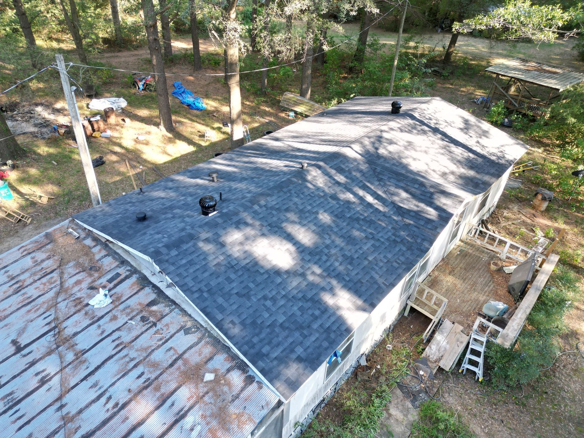 Overhead view of a house with a new dark shingle roof, surrounded by trees and a deck.