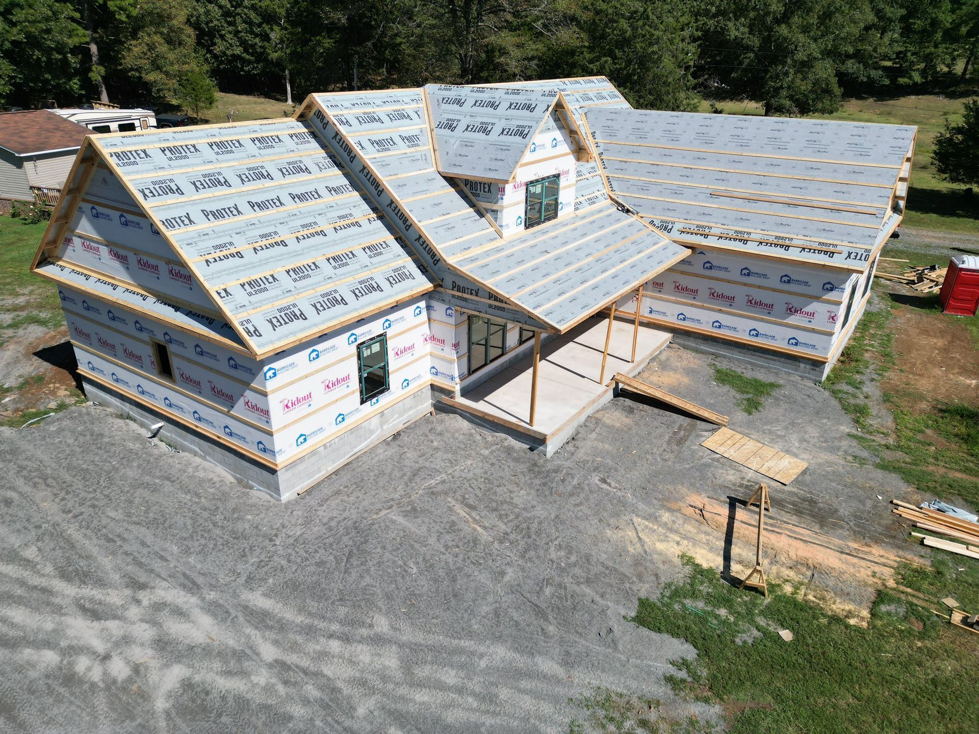 House under construction; gray gravel base, blue wrap on walls, light gray roof with protective covering.