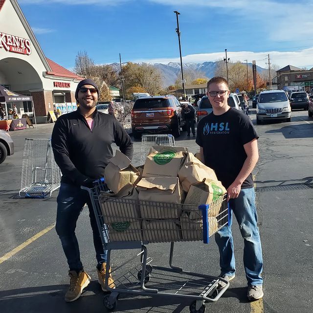 A man wearing an amsl shirt is standing next to a man pushing a shopping cart