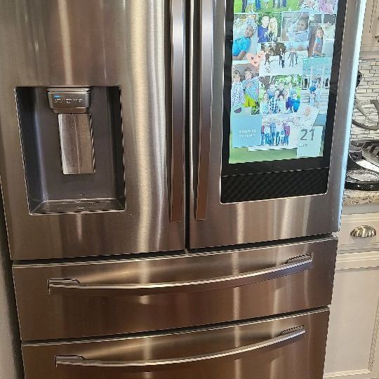 A stainless steel refrigerator with a large screen on the door.