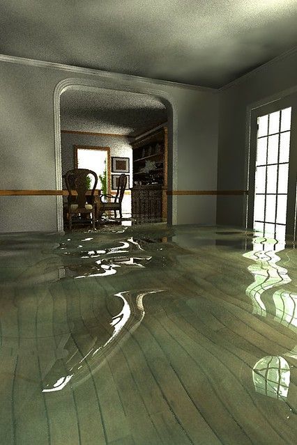 A flooded room with a wooden floor and a dining room in the background.