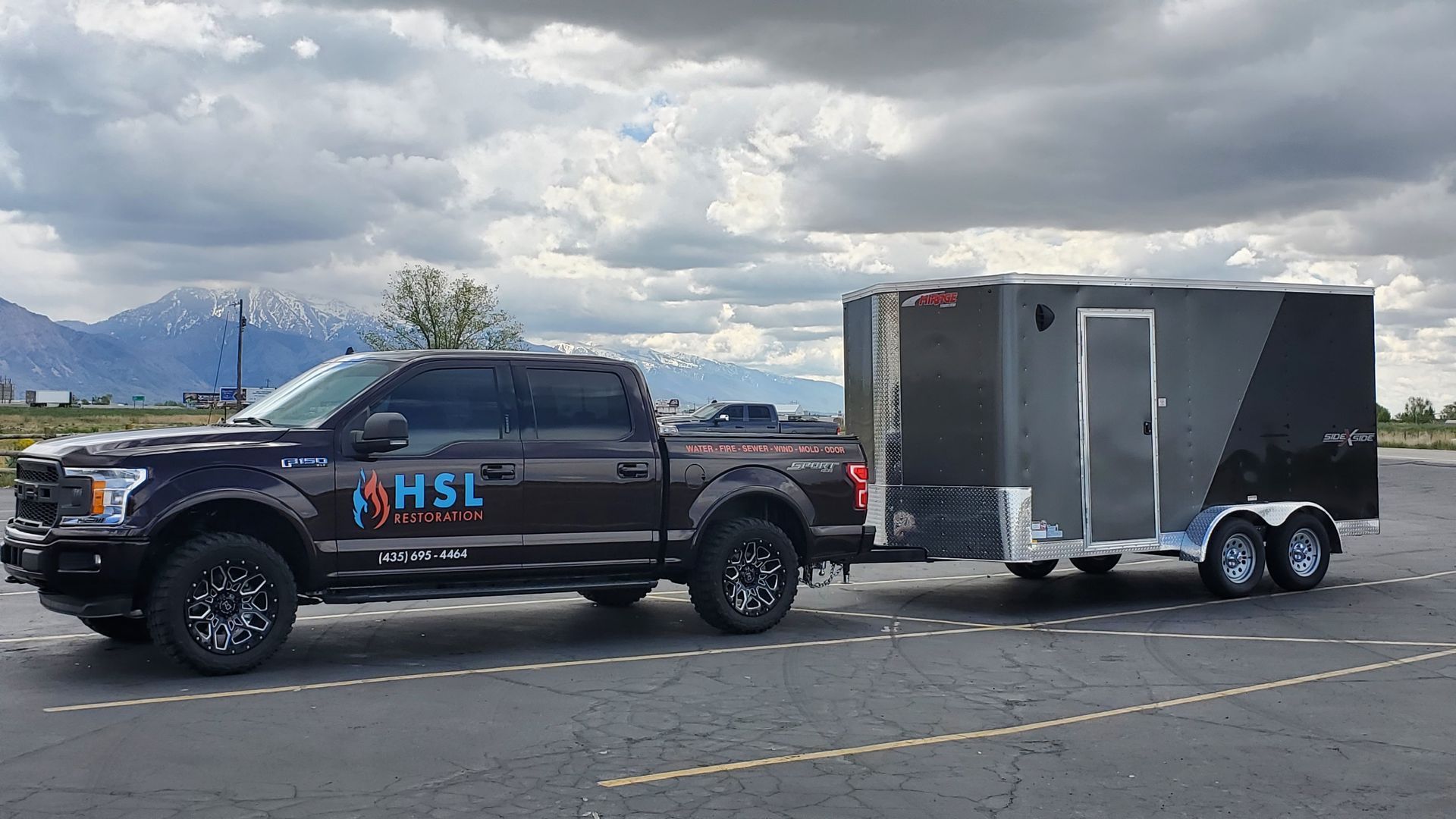 A black truck is pulling a trailer in a parking lot.