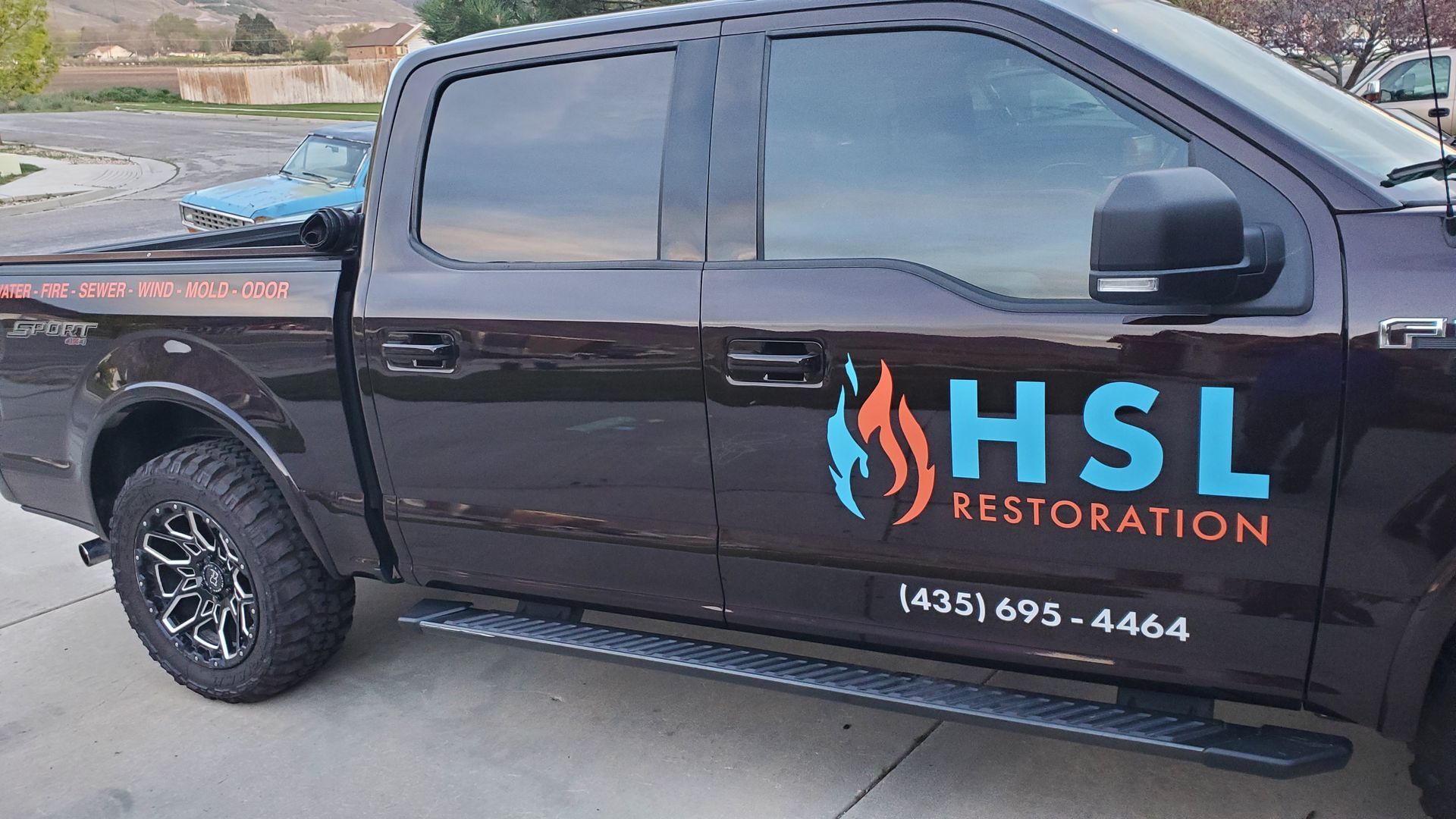 A black truck with the word hsl restoration on the side is parked in a parking lot.