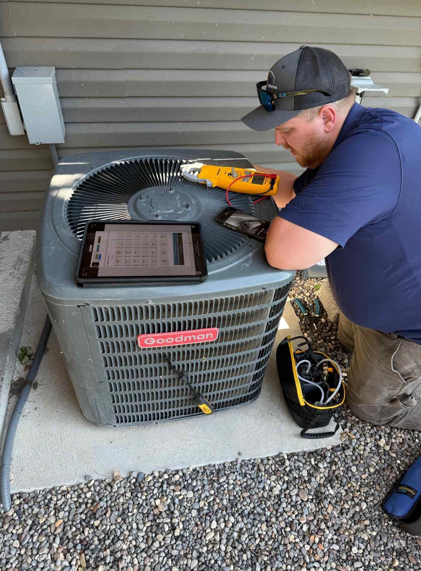 HVAC technician working on an air conditioner unit outside a house, using a tablet and tools.