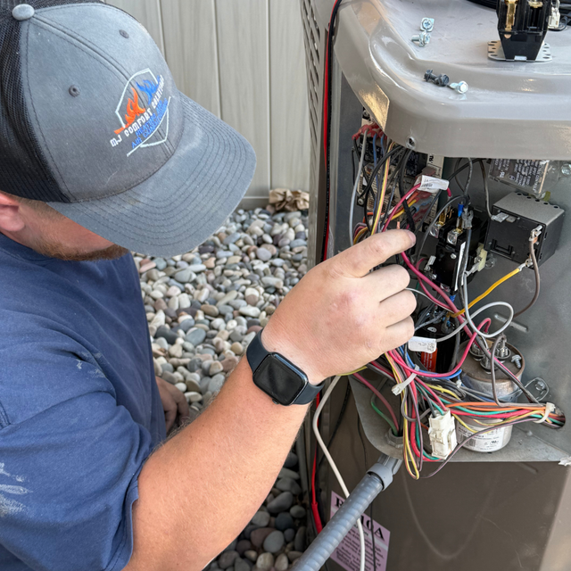 HVAC technician working on outdoor unit's electrical components, wearing a hat and smartwatch.
