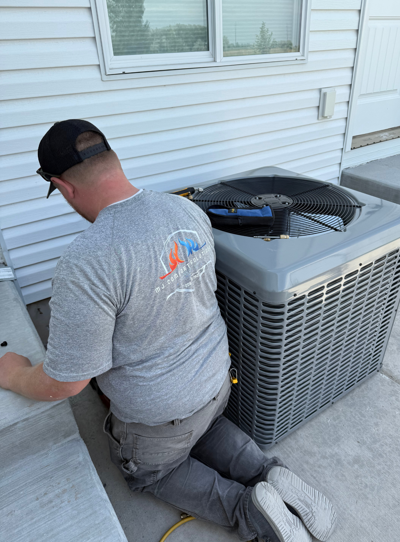 Man inspecting an AC unit with a flashlight near a window on a sunny day.