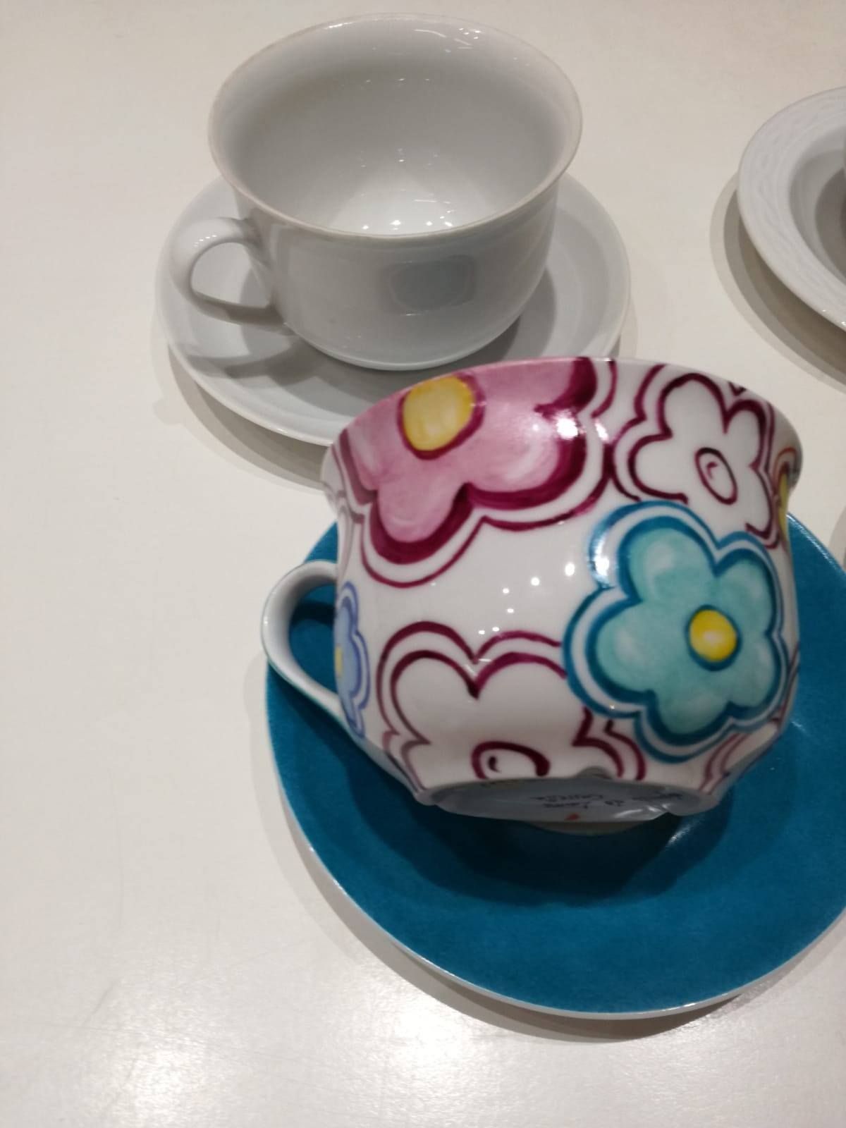 Tazze da tè bianche e floreali su piattini, appoggiate su una superficie bianca. 