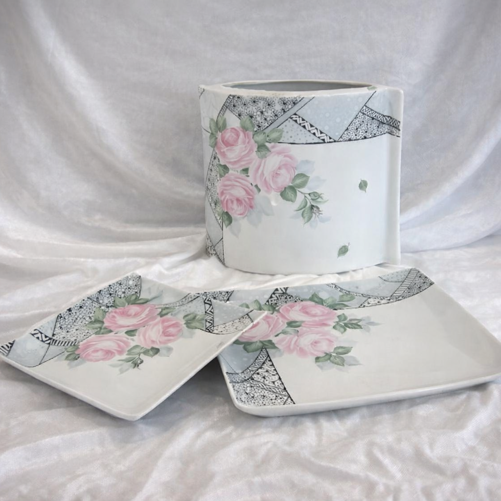 Vaso e piatti in ceramica bianca con motivo a rose rosa su un panno bianco.