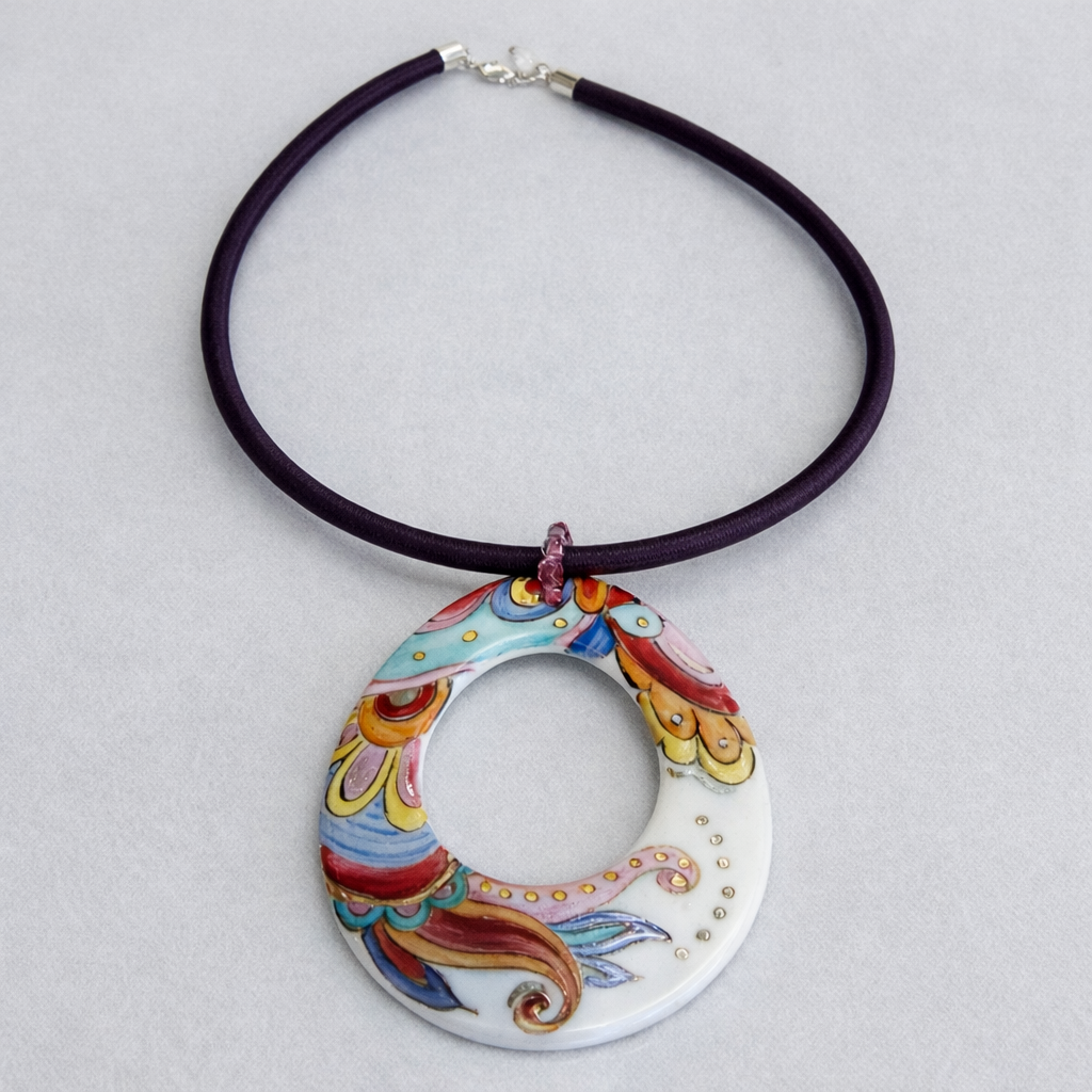 Collana con pendente ovale con motivo floreale colorato, su cordino viola scuro.