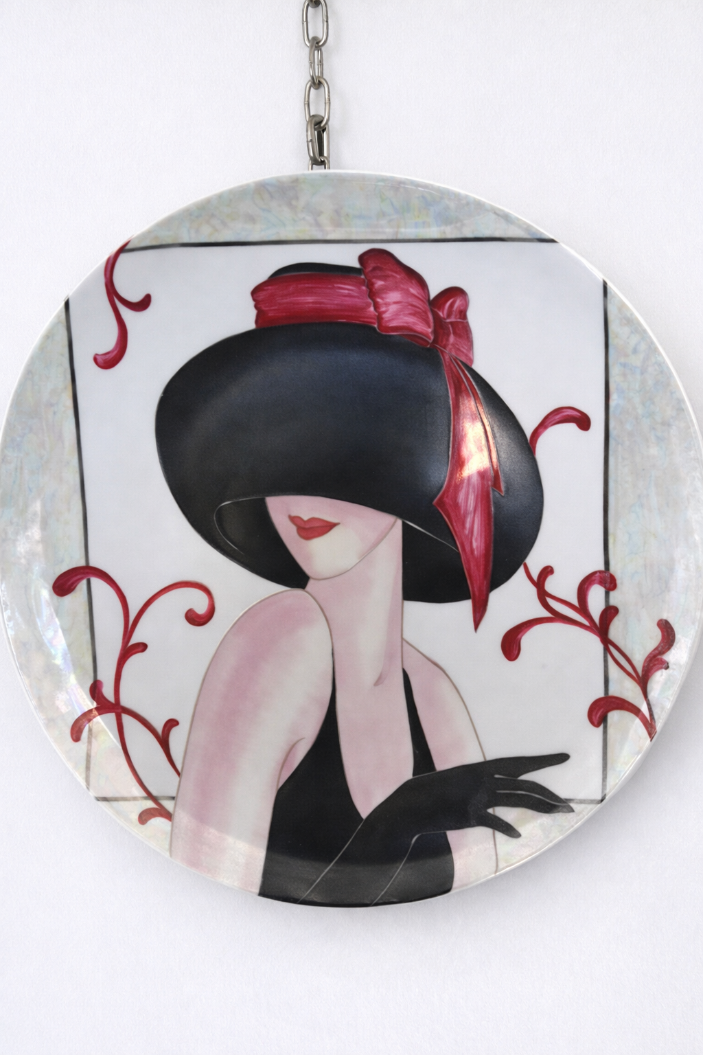 Donna con cappello nero e fiocco rosso, abito nero e guanti su un piatto decorativo con ghirigori rossi.