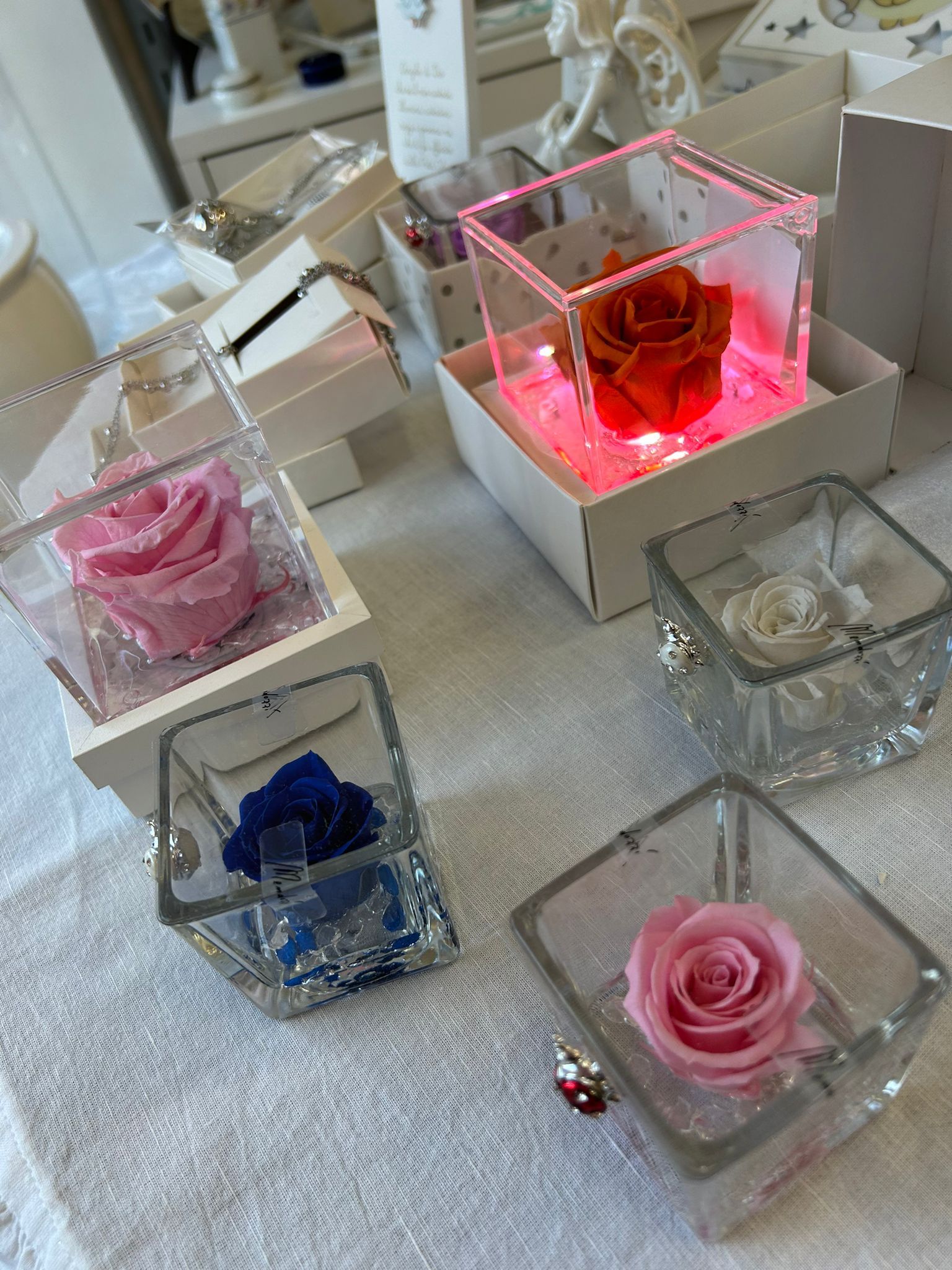 Composizione di rose colorate racchiuse in scatole trasparenti, alcune illuminate con luci LED, su una superficie bianca.