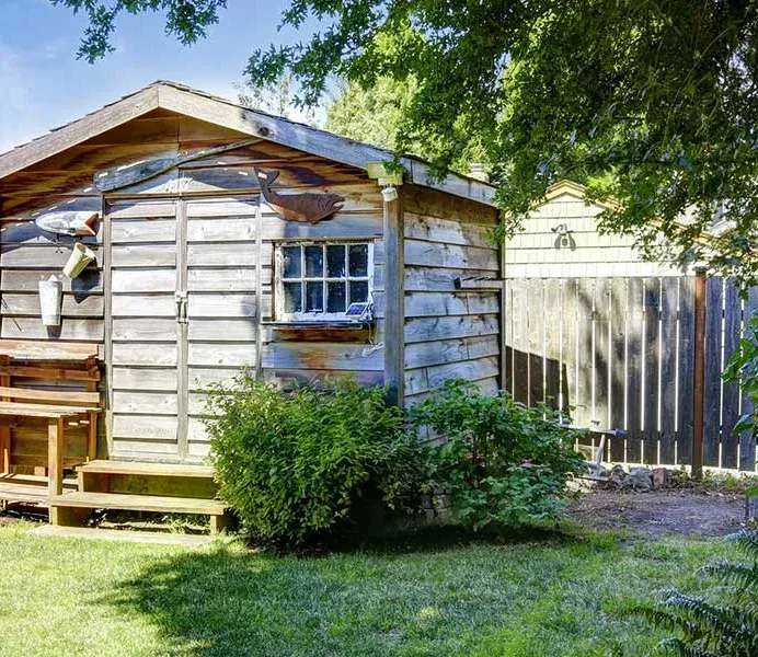 A small wooden shed with a window and a bench in the backyard.