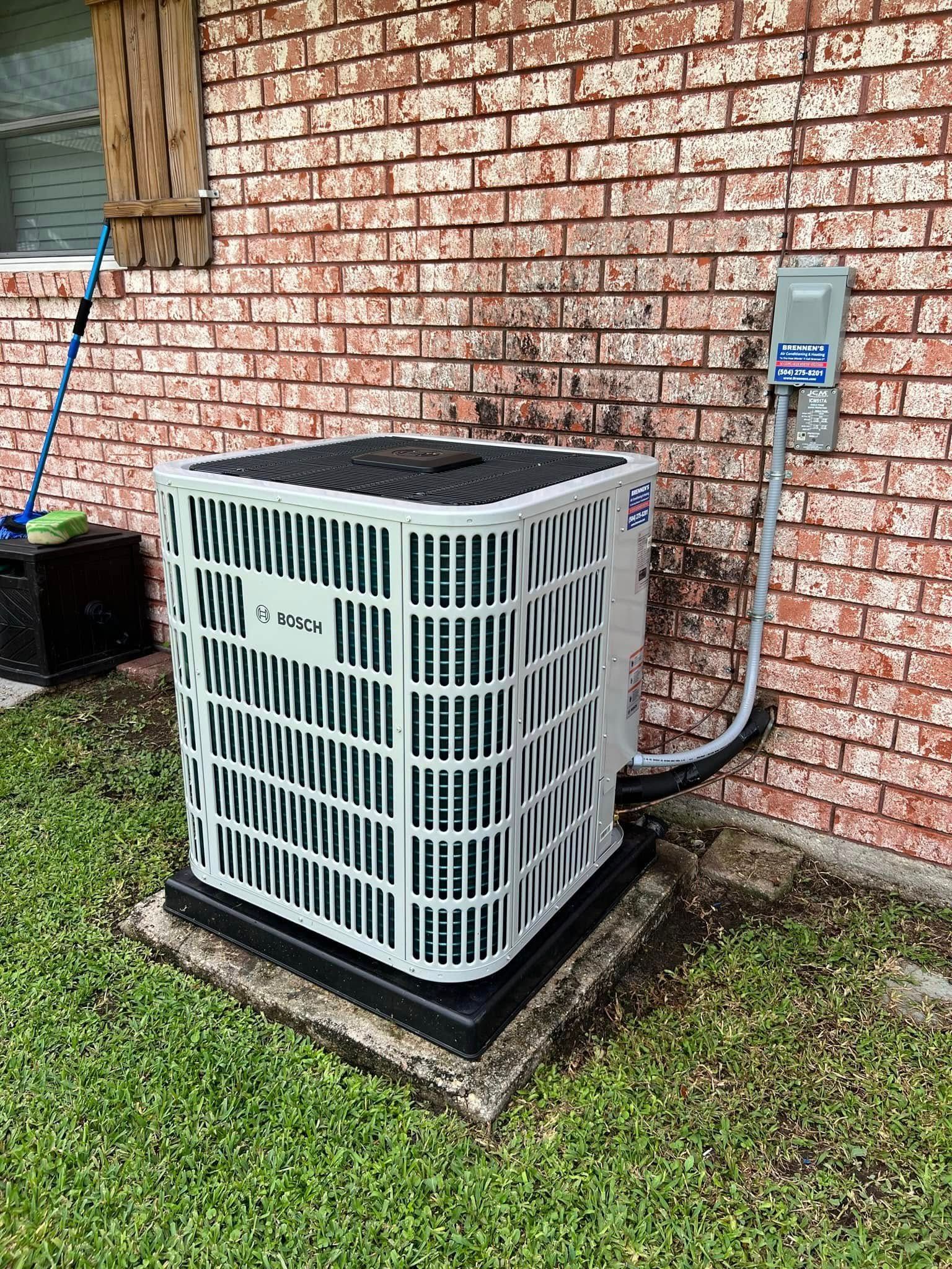 An air conditioner is sitting on the side of a brick building.