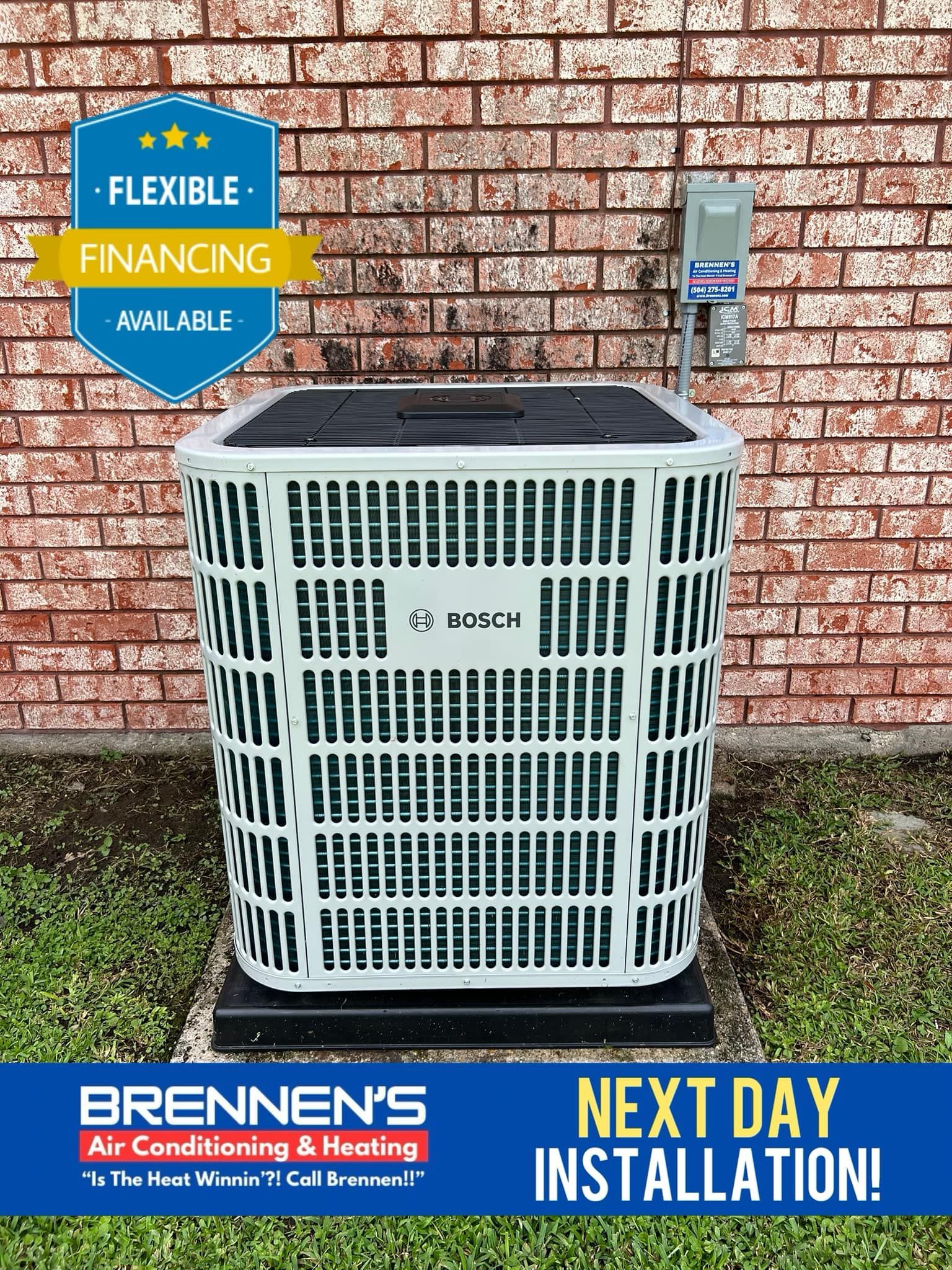 A white air conditioner is sitting in front of a brick wall.