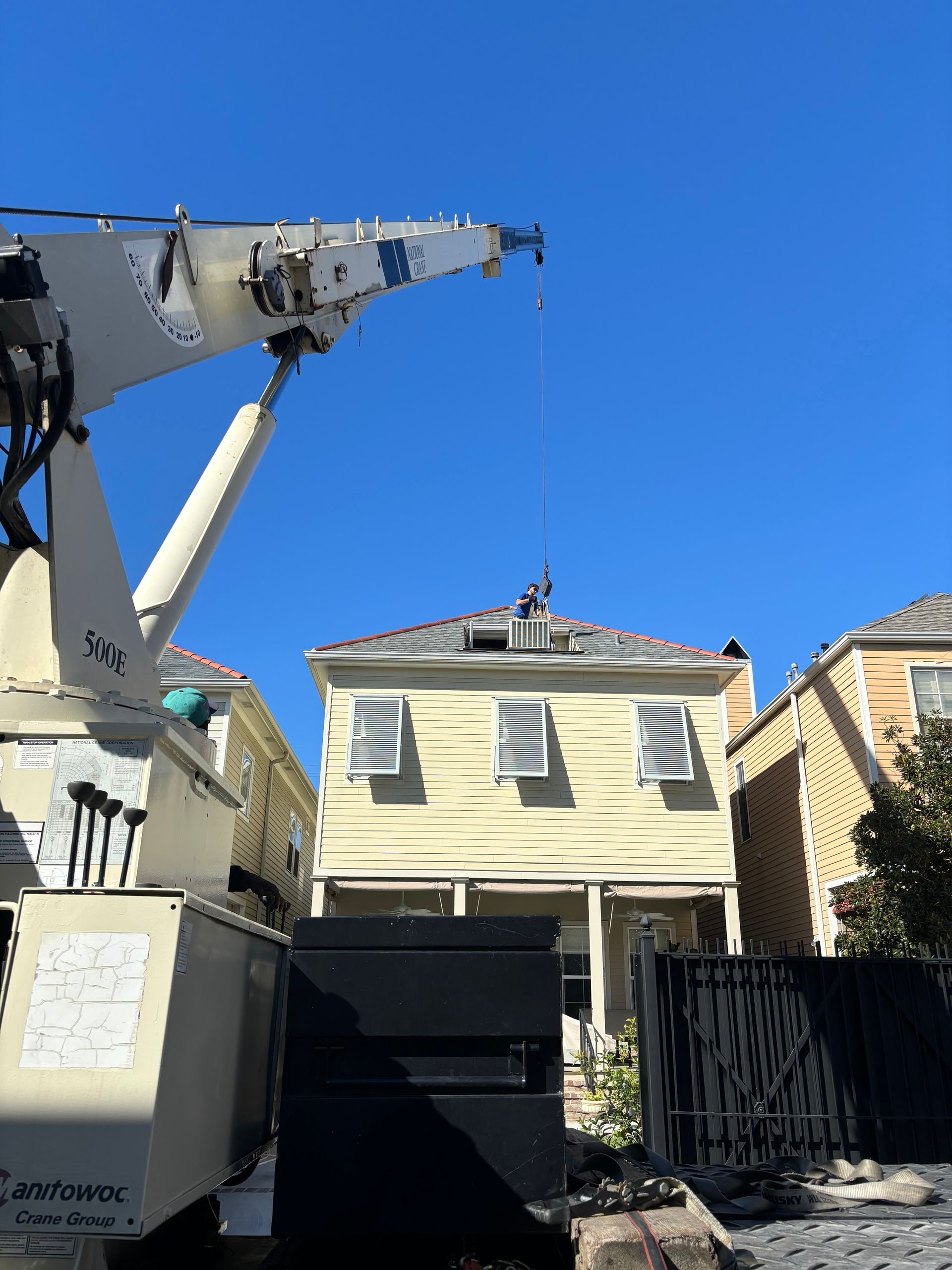 A crane is being used to remove a tree from the roof of a house