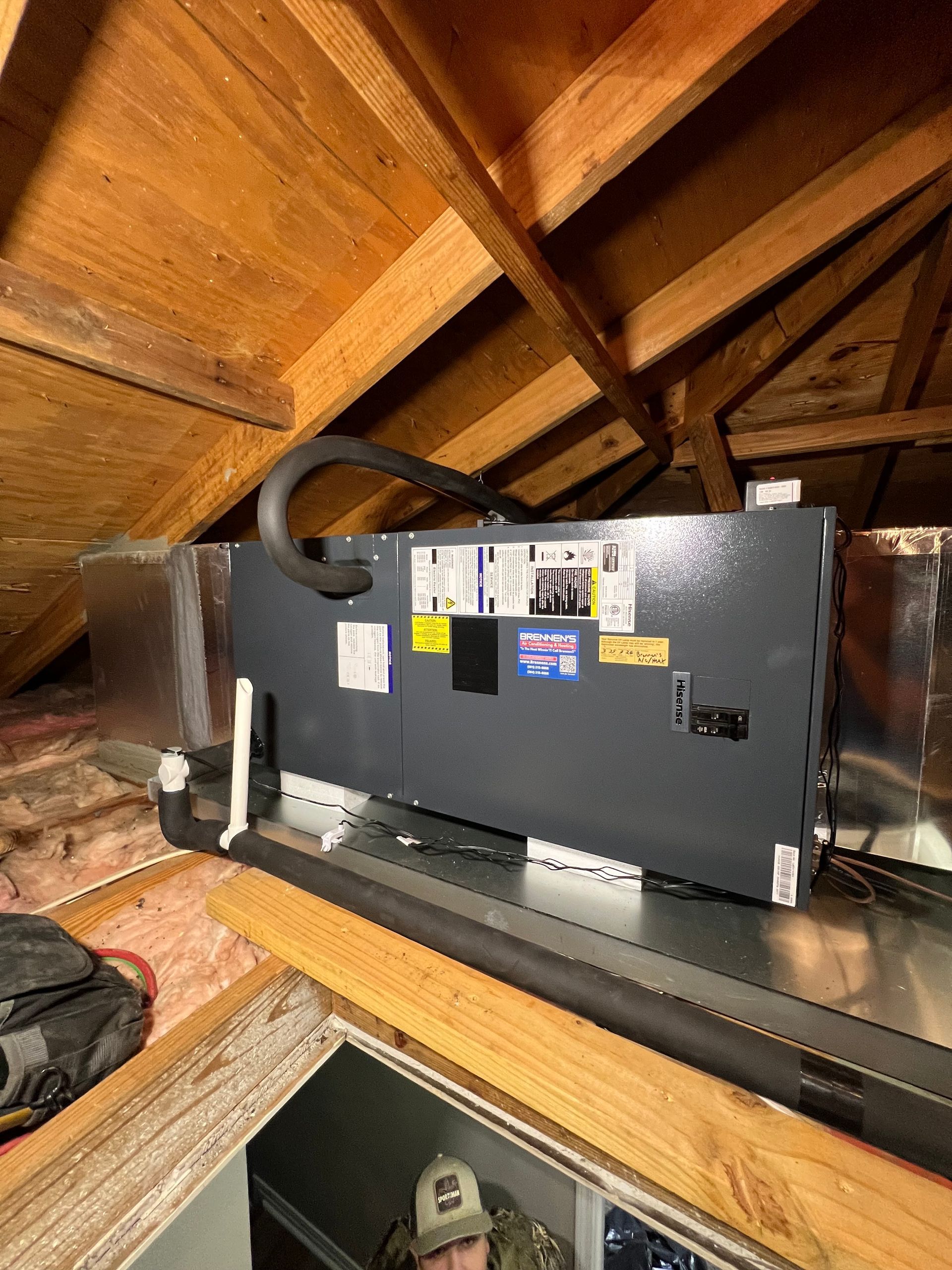 A man is working on an air conditioner in the attic of a house.