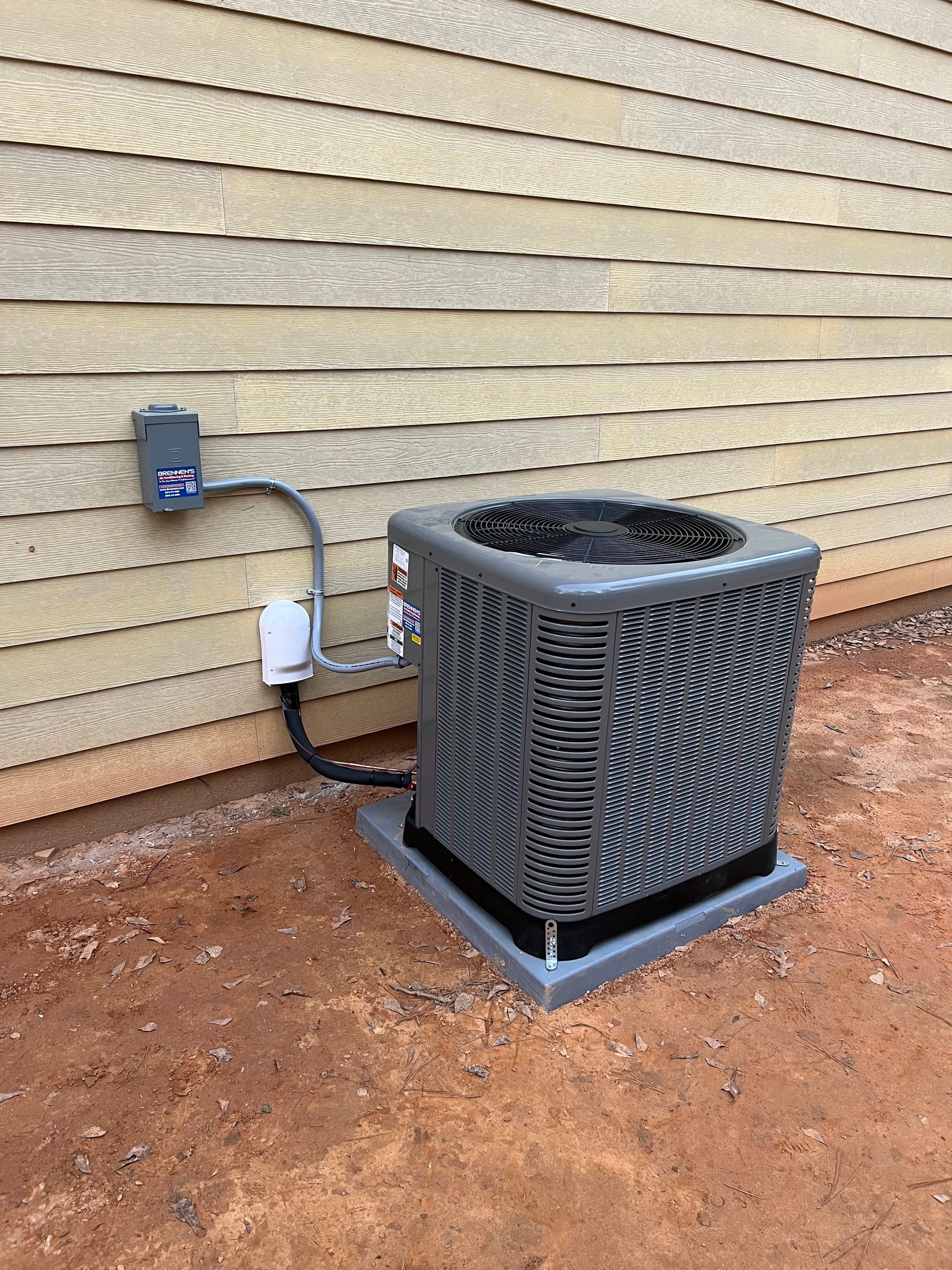 A gray air conditioner is sitting on the ground next to a house.