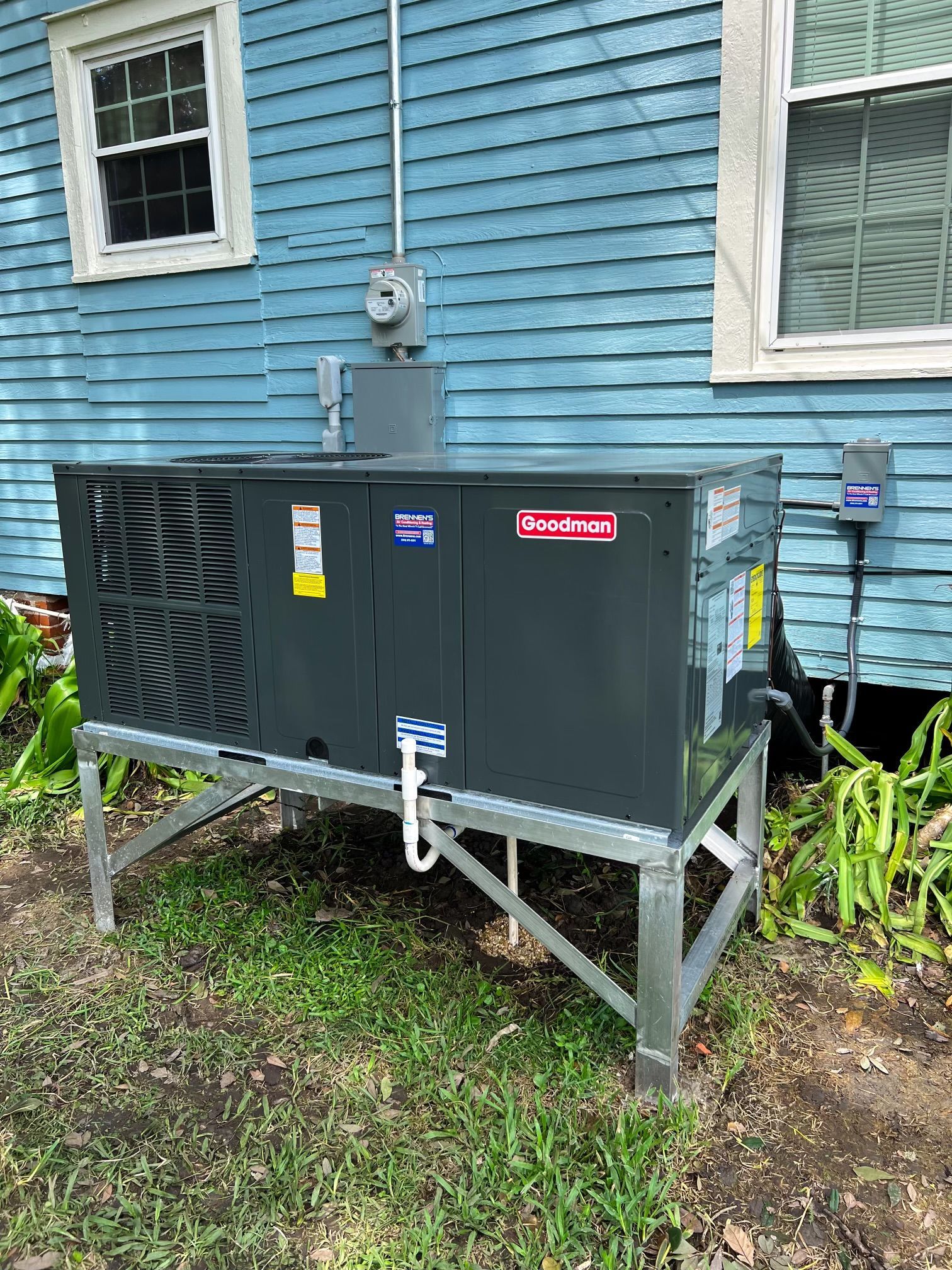 A large air conditioner is sitting in front of a blue house.