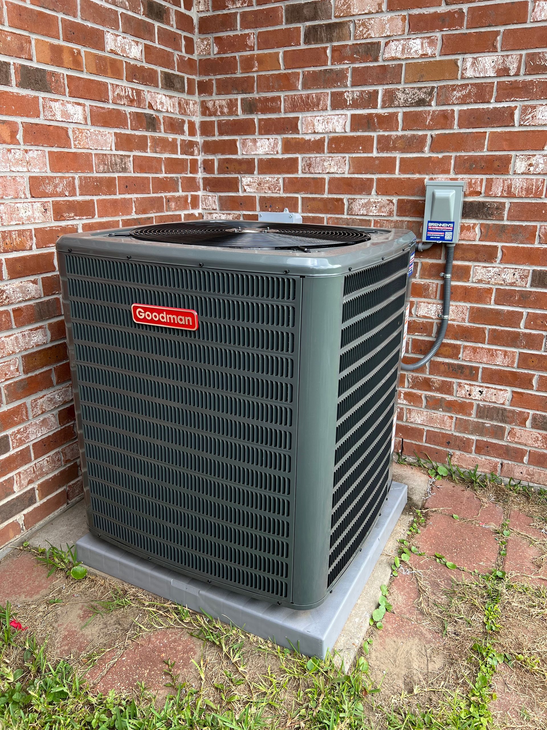 An air conditioner is sitting in the corner of a brick building.
