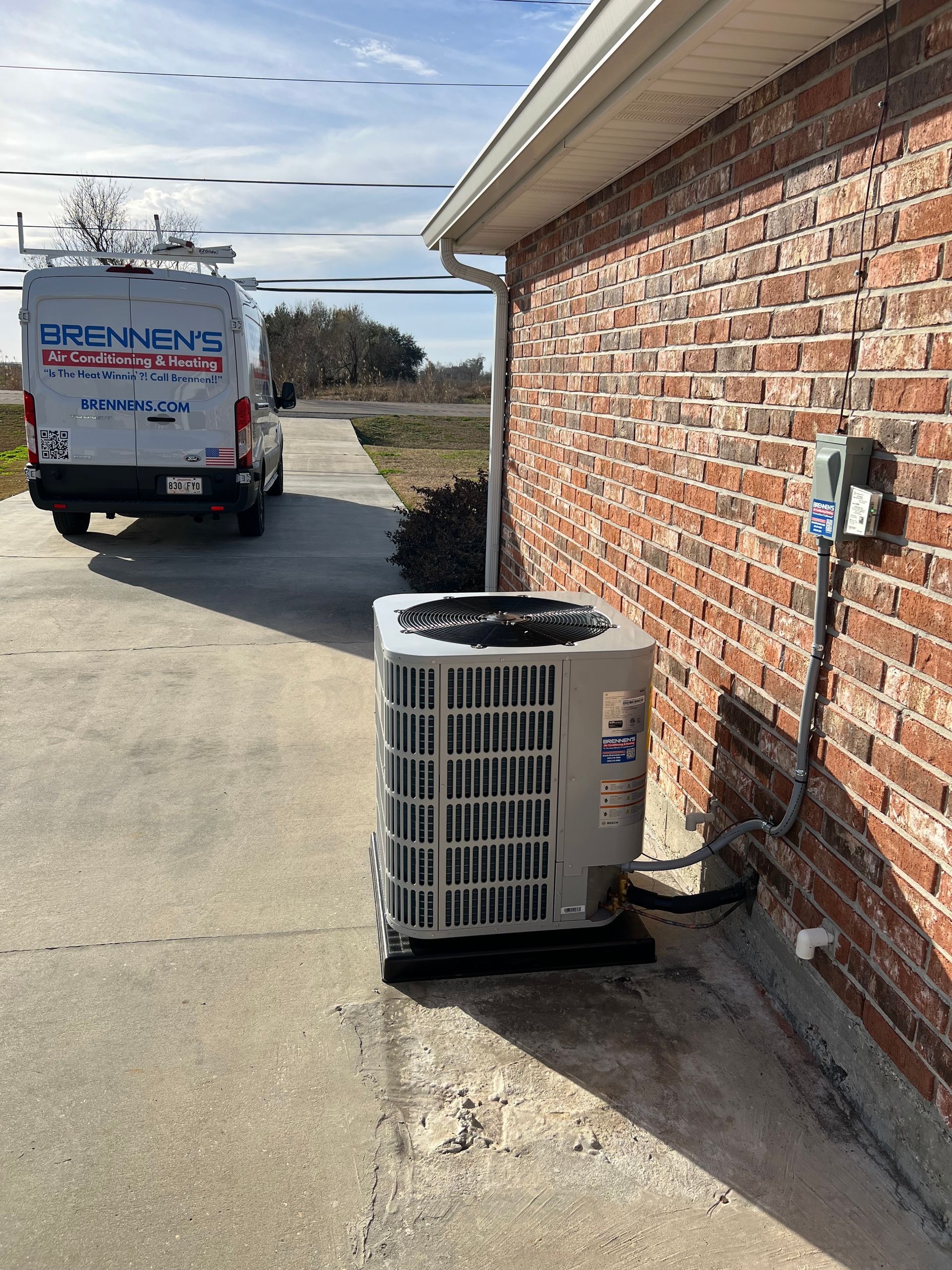 A van is parked on the side of a brick building next to an air conditioner.