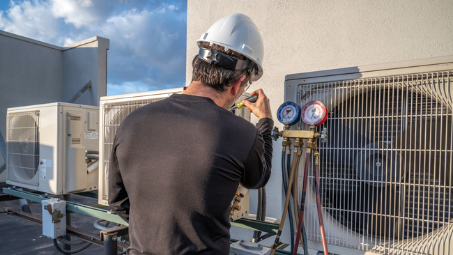 A man is working on an air conditioner on the roof of a building.