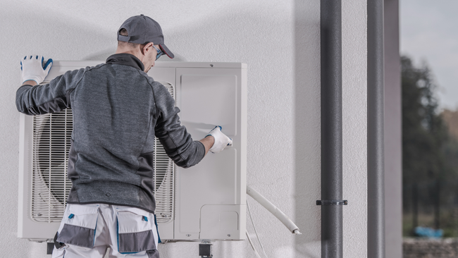 A man is installing an air conditioner on the side of a building.