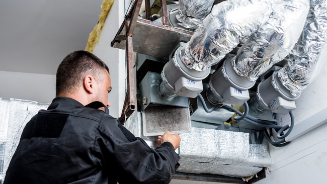 A man is working on a ventilation system in a building.