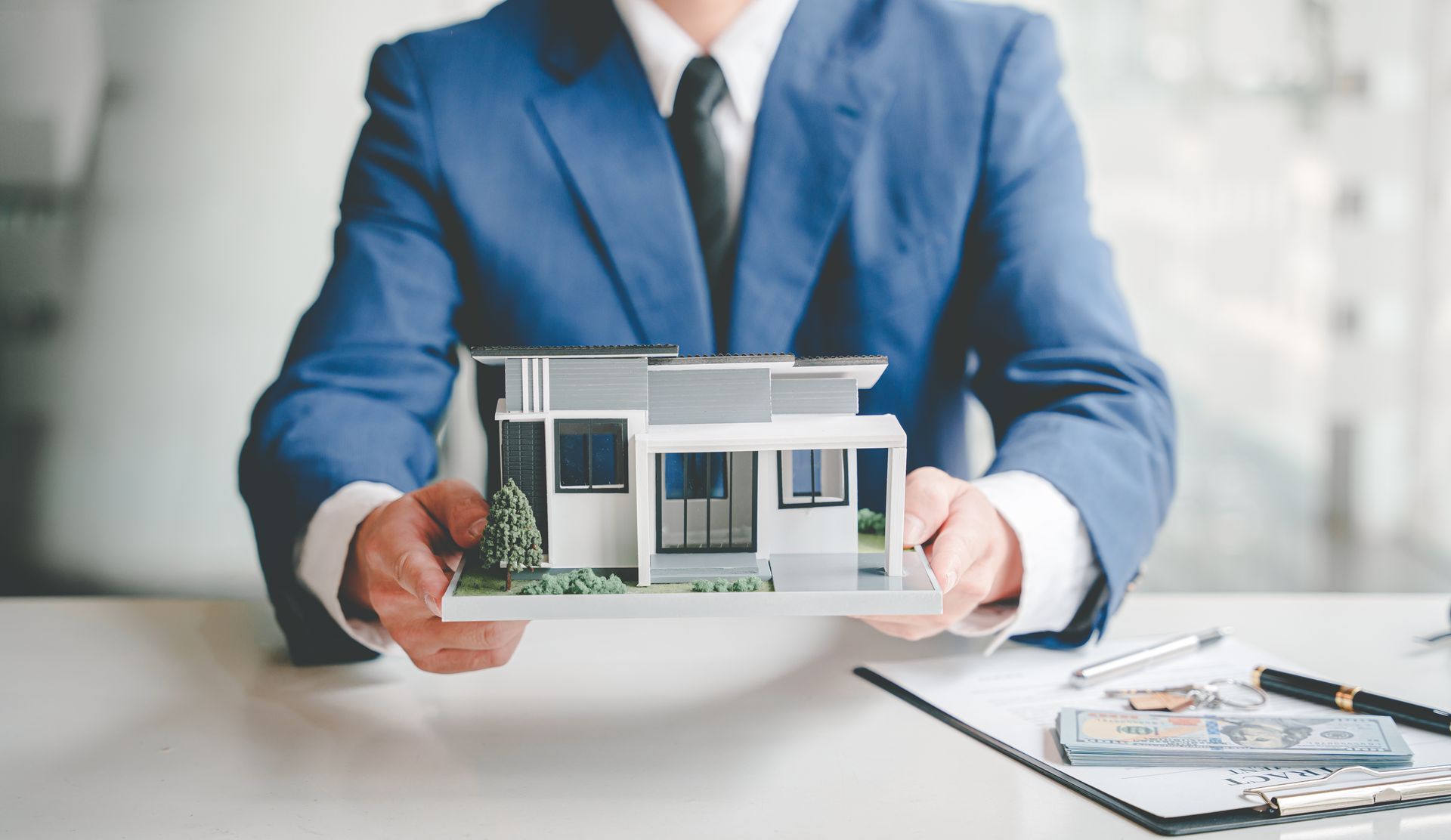 A man in a suit and tie is holding a model of a house.