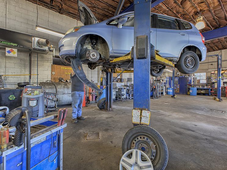 Car lifted in a garage on a repair hoist, with a mechanic working underneath. | Allwine Curry Inc