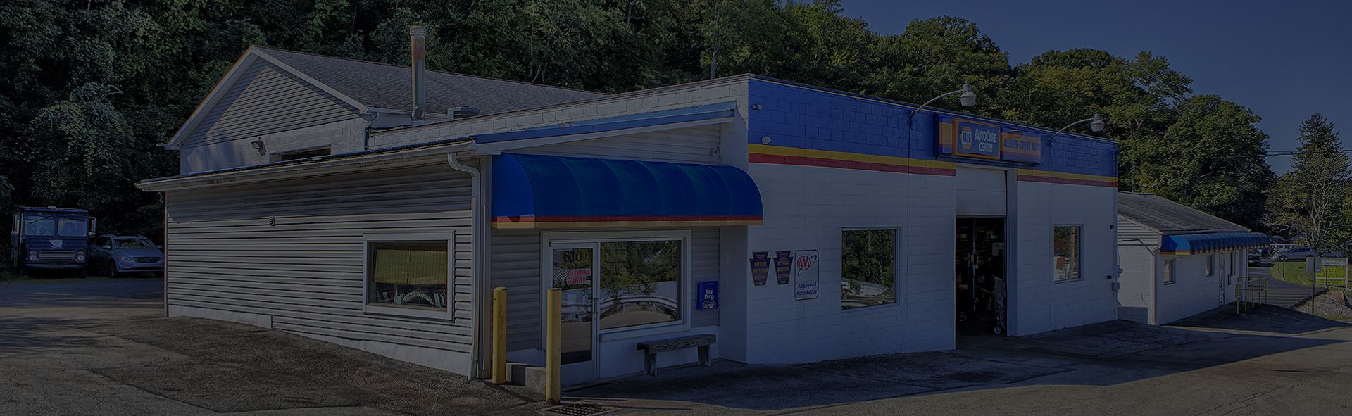 Small white building with blue awnings and roof trim under bright sunlight, with trees behind it | Allwine Curry Inc