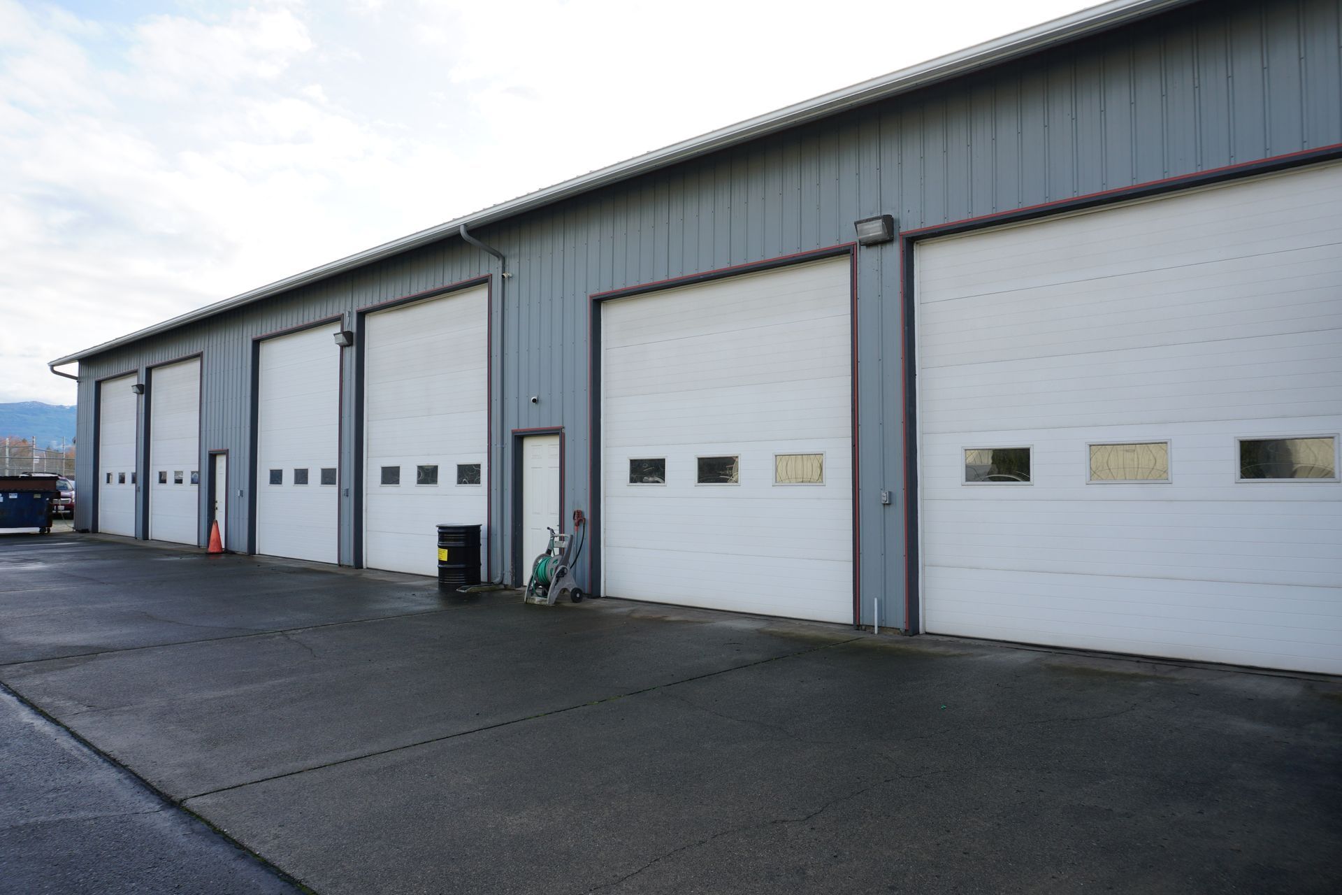 Gray building with four large garage doors, asphalt parking area.