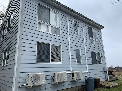 Two-story, light-blue sided building with multiple windows, outdoor AC units, and a gray sky.