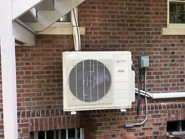 White air conditioning unit on a red brick wall beneath stairs.