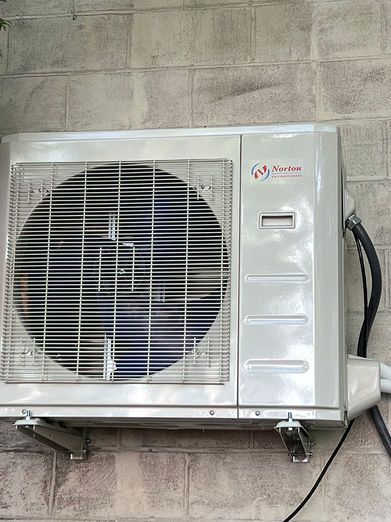 Outdoor air conditioning unit mounted on a brick wall, with fan visible.