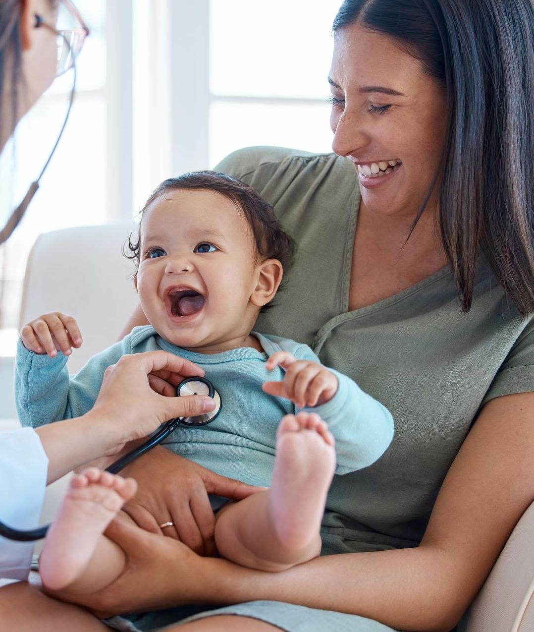 Doctor listening to baby's heart with stethoscope, mother smiling.