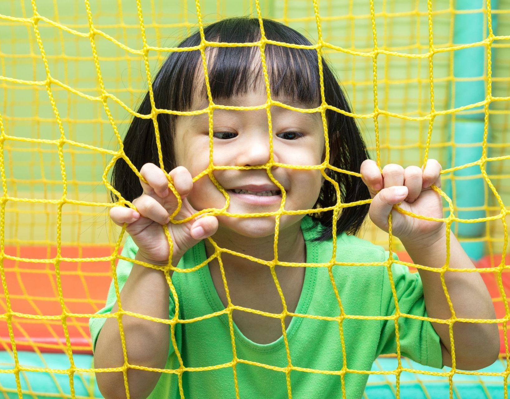 A young girl behind a soccer goal net, grasping the net.