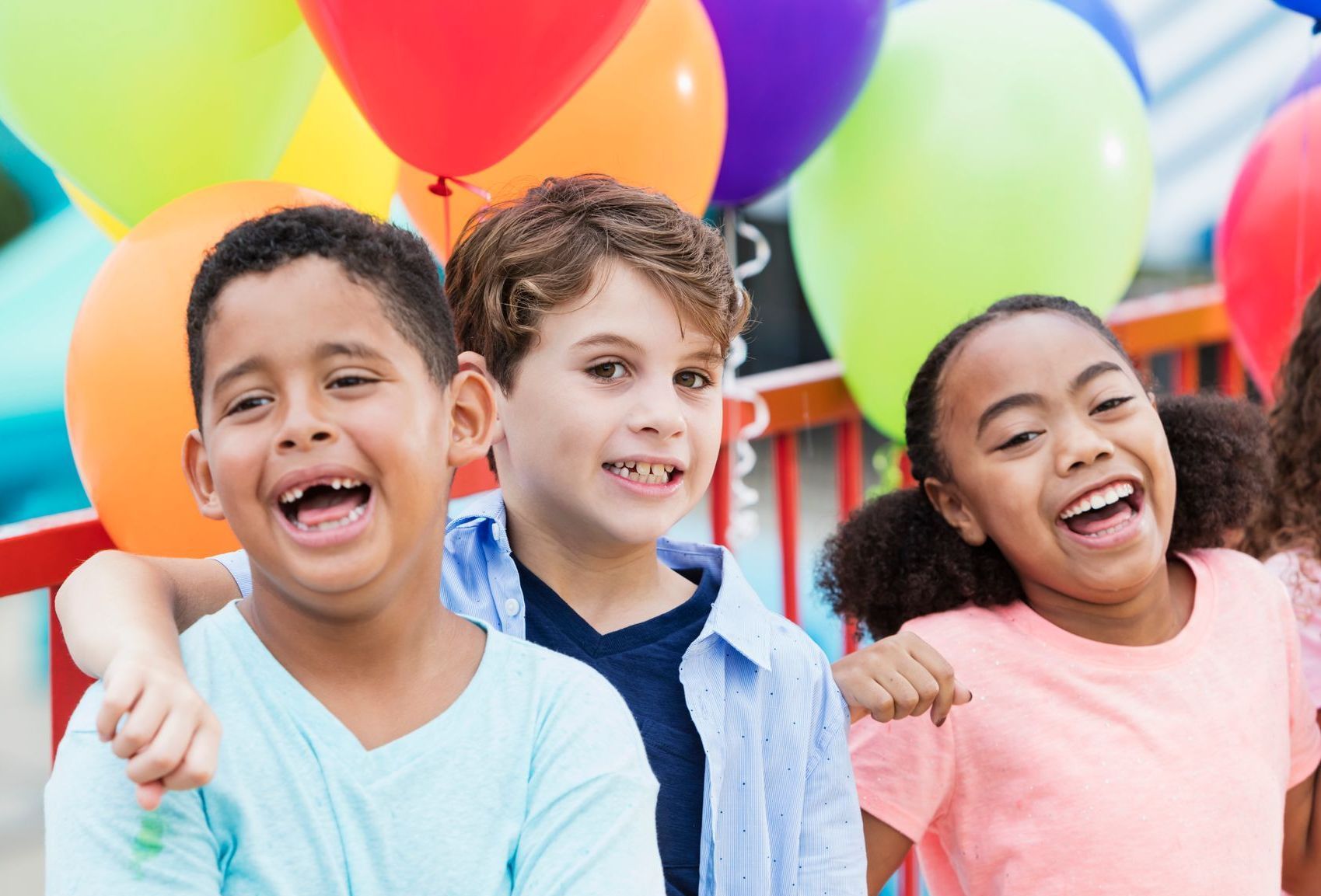 Three laughing children with balloons behind them.