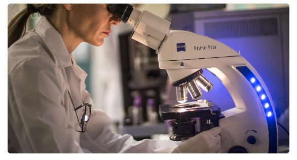 Una mujer está mirando a través de un microscopio en un laboratorio.