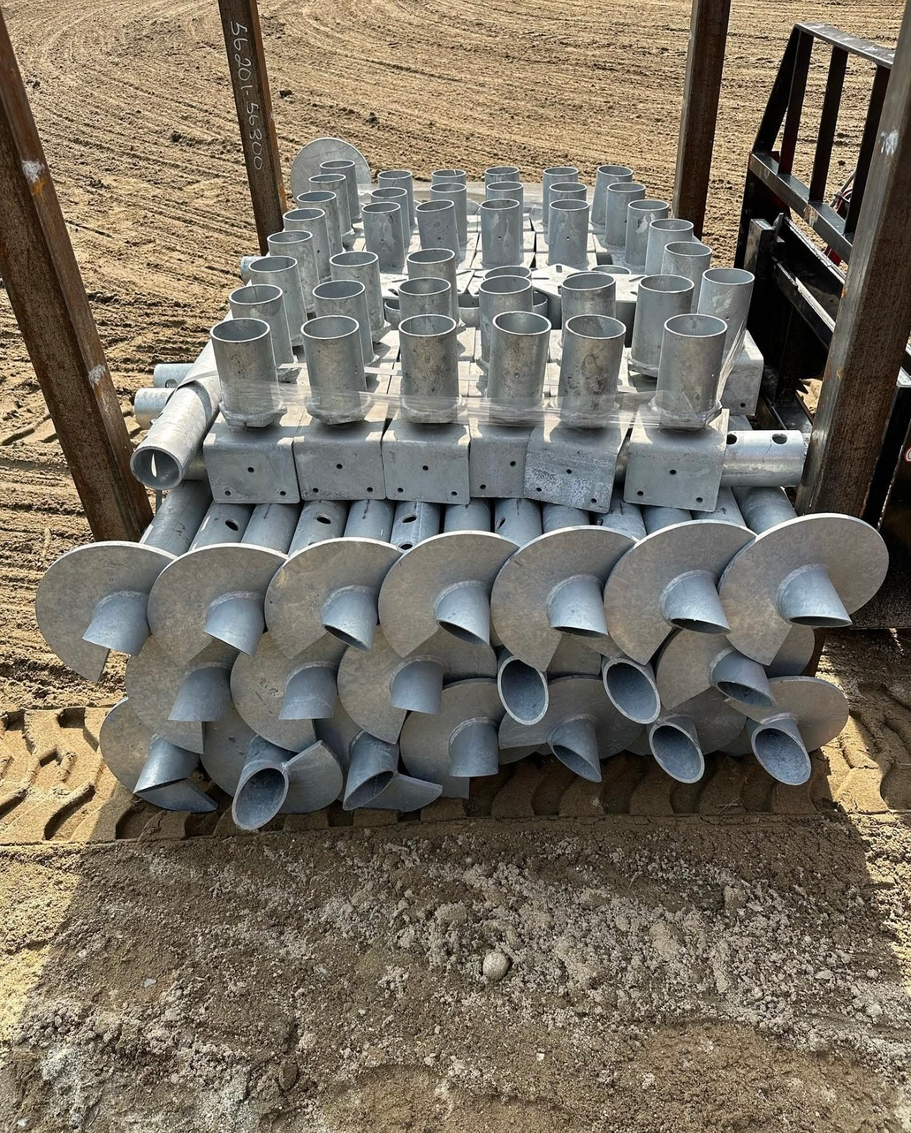 A stack of galvanized steel helical piles with large, corkscrew-shaped bases arranged on the ground.