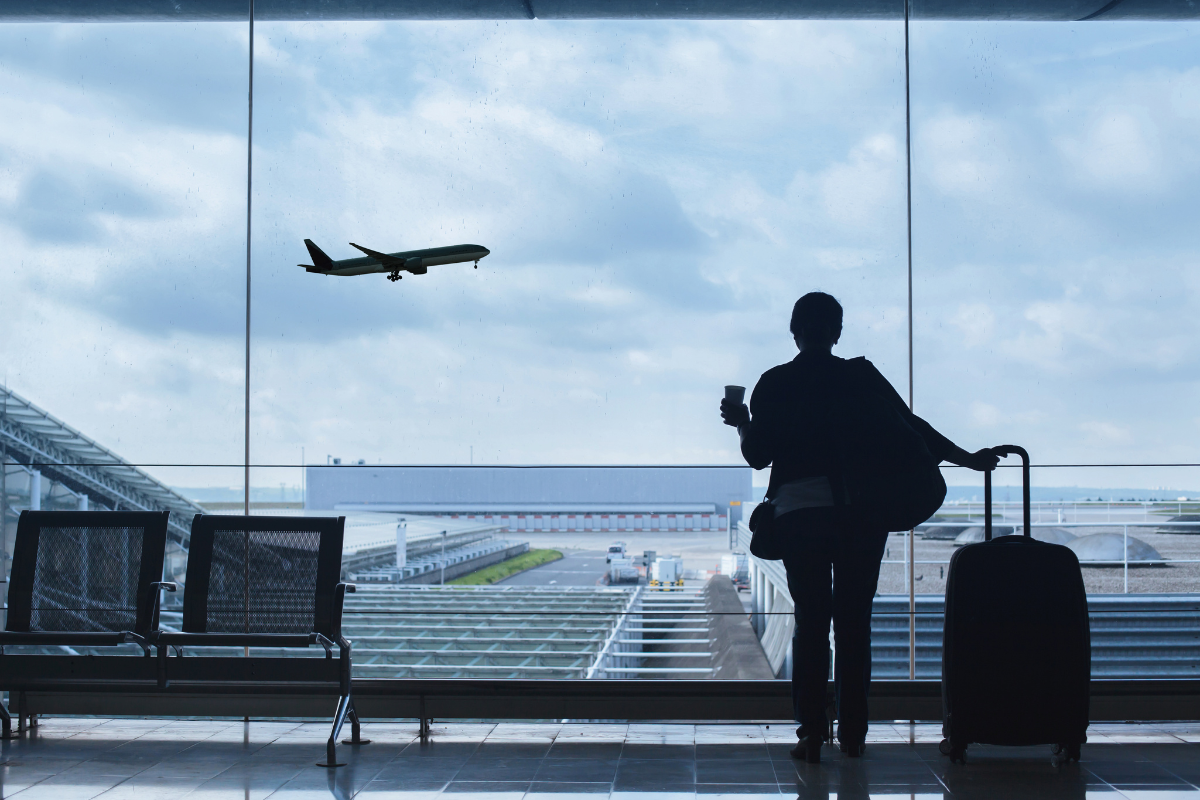 a woman with a suitcase is looking out of a window at an airplane taking off .