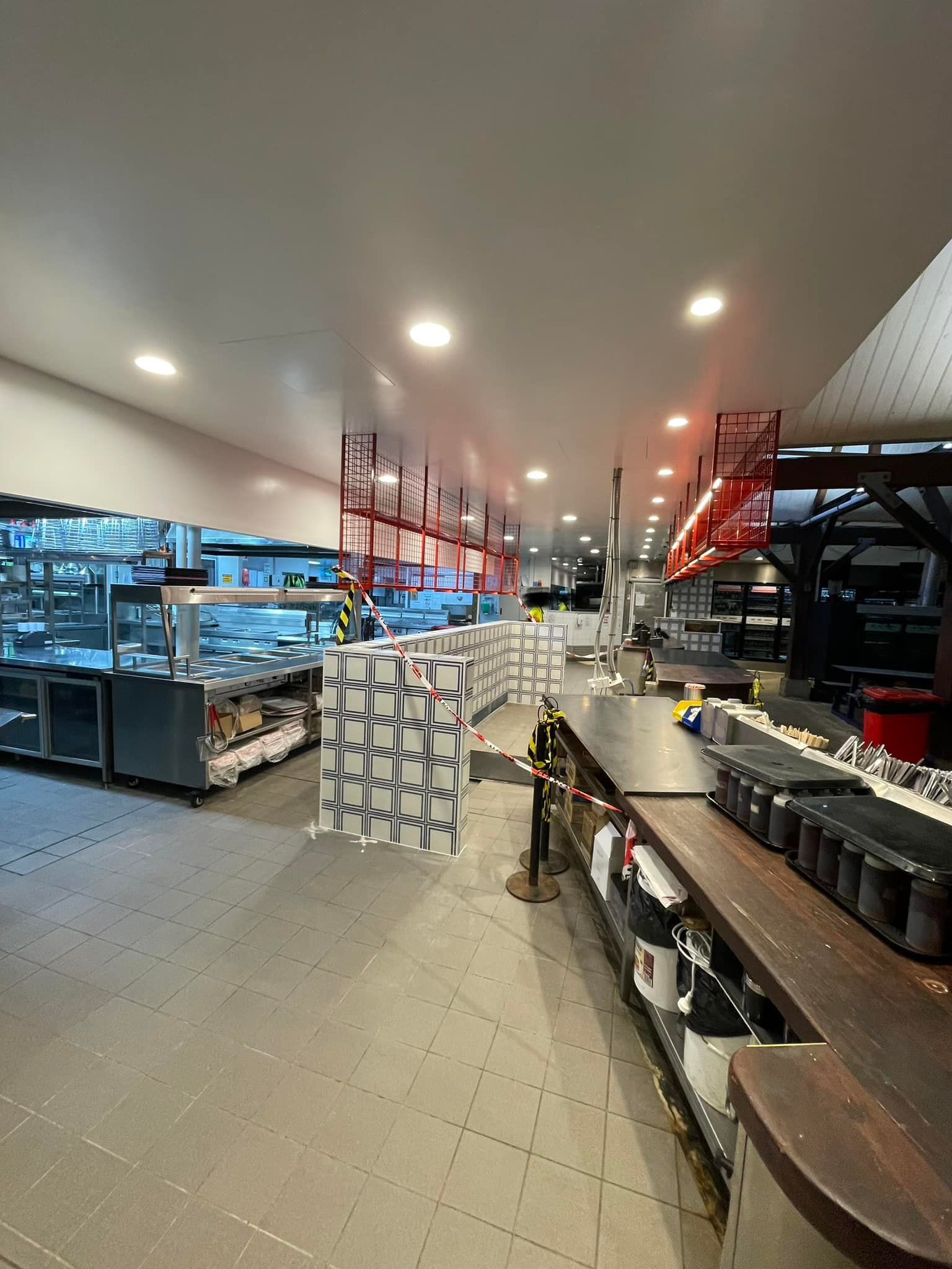 Interior of a commercial kitchen, possibly under construction. Stainless steel appliances and a bar area are visible.