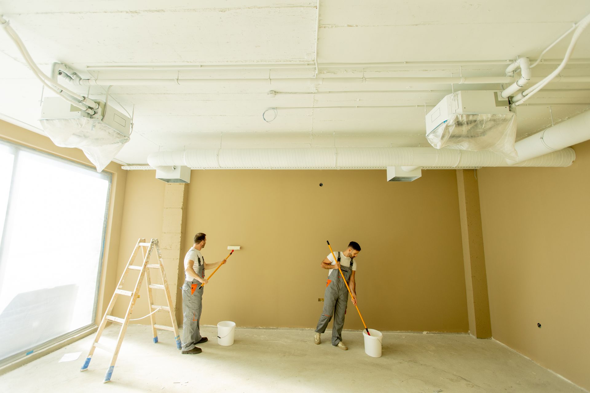 Commercial painters, painting an interior wall in a commercial space during daylight hours. Commercial painters, painting an interior wall in a commercial space during daylight hours.
